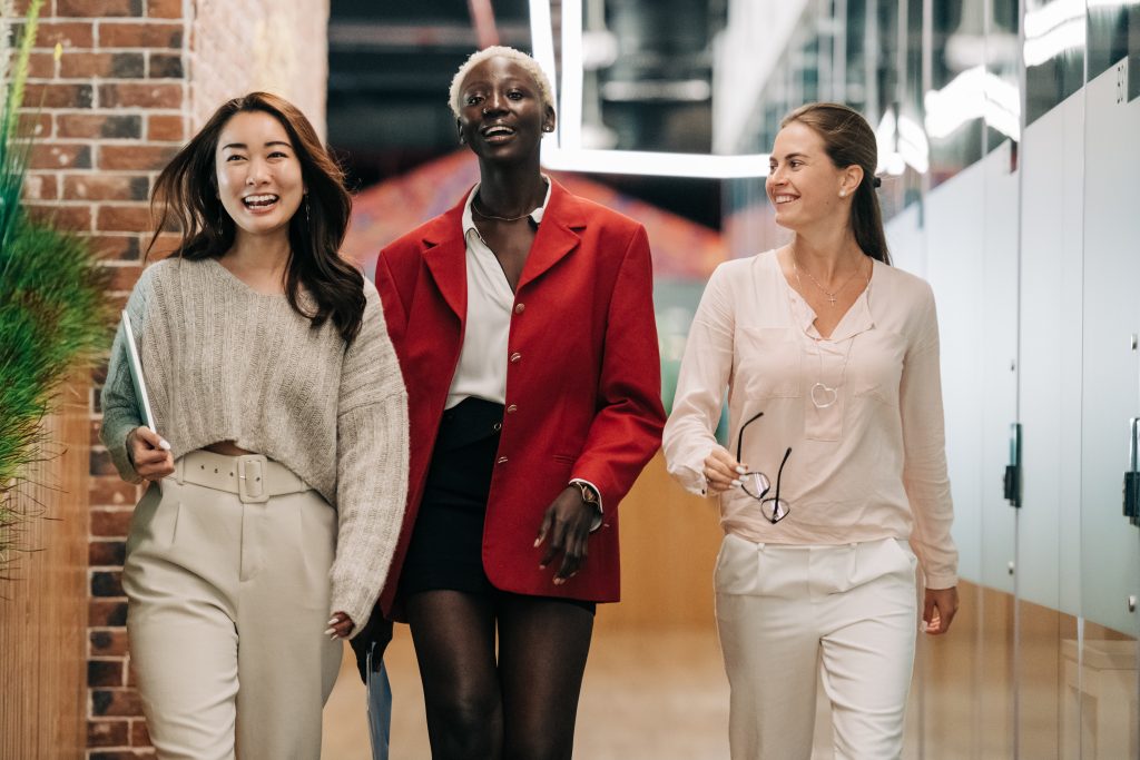 Photo of three professional women walking down a hall in the workplace smiling.